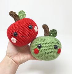 two knitted apples with faces on each one being held by someone's hand