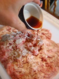 a person pouring sauce on top of a hamburger pattie covered in ketchup