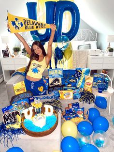 a woman holding up a sign in front of a table filled with blue and yellow balloons