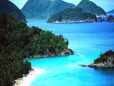 an island with several small islands in the water and people swimming on the beach below