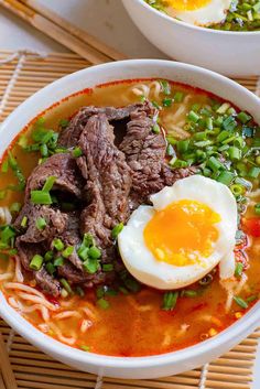 a bowl of soup with meat, noodles and an egg on the side next to chopsticks