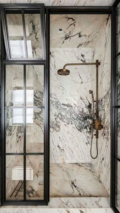 a walk in shower sitting next to a glass door and tiled floored bathroom with marble walls