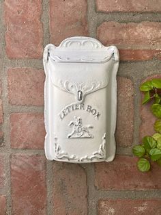 a brick wall with a white mailbox attached to it's side next to a green plant