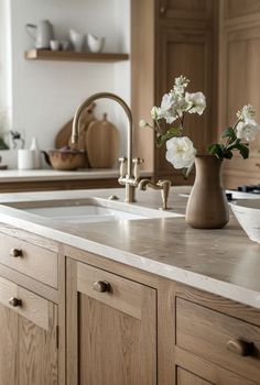 a kitchen with wooden cabinets and white flowers in a vase on the sink countertop