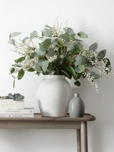 a white vase filled with flowers on top of a wooden table next to two books