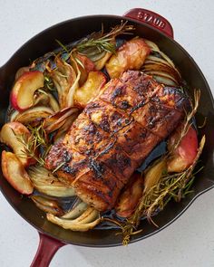 a pan filled with meat and vegetables on top of a white countertop next to utensils