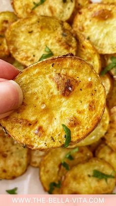 a hand holding up a potato wedge with herbs on top