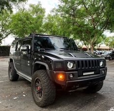 a black hummer truck parked in a parking lot with trees and cars behind it