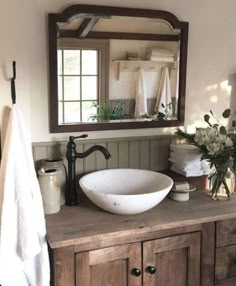 a bathroom sink sitting under a mirror next to a wooden cabinet and white towels on top of it