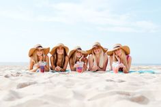 four beautiful young women laying on top of a beach next to each other holding drinks