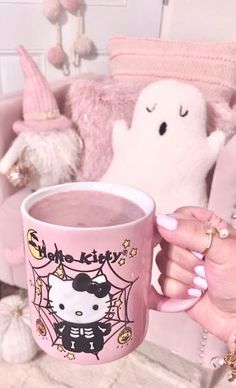 a person holding a pink coffee cup with hello kitty on it and two stuffed animals in the background