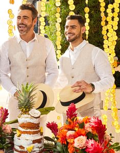 two men standing next to each other in front of a cake with pineapples on it