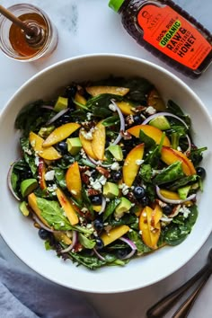 a white bowl filled with salad next to two spoons and an orange juice bottle