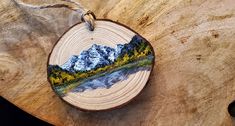 a wooden ornament with a mountain scene painted on it