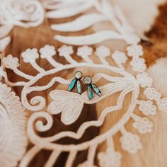 two pairs of earrings sitting on top of a piece of lace covered fabric with flowers and leaves