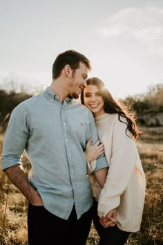 a man and woman are standing together in the grass with their arms around each other