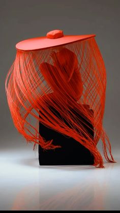 an orange hat with long red hair on top of a black box in front of a gray background