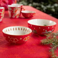 red and white bowls sitting on top of a table next to pine branches with green leaves