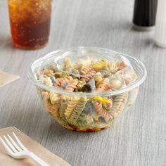 a plastic bowl filled with pasta and veggies next to a cup of soda