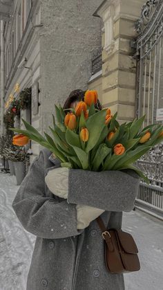 a woman is walking down the street with flowers in her hand and wearing a coat