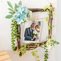 a photo frame with flowers and greenery hanging on the wall