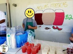 two men standing behind a table with cups and drinks on it that have smiley faces drawn on them