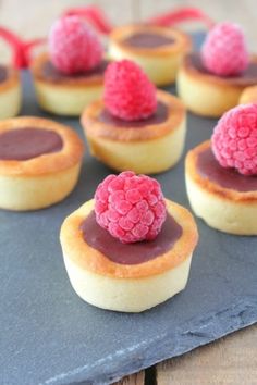 small desserts with raspberries and chocolate sauce on top are sitting on a slate platter