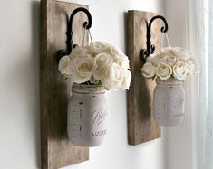 two mason jars with flowers are hanging on the wall