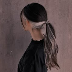 a woman with long grey hair wearing a black shirt and braided ponytail, standing in front of a concrete wall