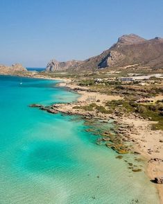 an aerial view of a beach with clear blue water and rocky mountains in the background