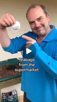 a man in blue shirt holding up a white object with words on it that read teabags from the supermarket