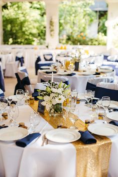 the tables are set with white and blue linens, gold chargers and centerpieces