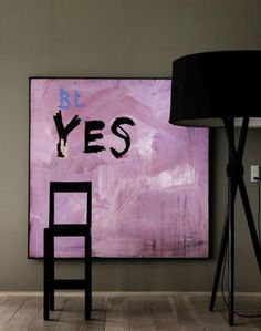 a chair sitting in front of a large painting on the wall next to a lamp