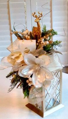 a christmas centerpiece with white flowers and greenery in a square metal container on a table