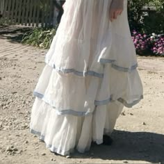 a woman in a white dress is standing on the dirt ground with her hands behind her back