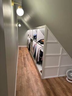 an attic bedroom with closets and clothes on shelves in the wall, along with hard wood flooring