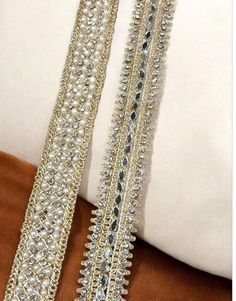 a pair of gold and crystal bracelets on a brown velvet pillow with white pillows in the background