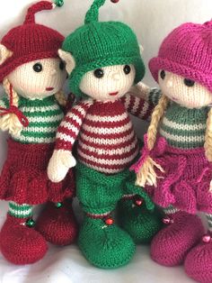 three knitted dolls sitting next to each other on a white surface with christmas decorations around them