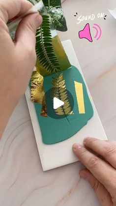 someone is making a card with gold foil and green leafy decorations on top of it