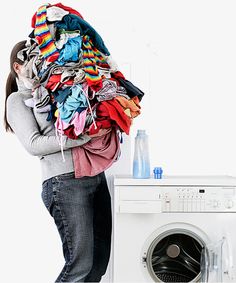 a woman is standing in front of a washing machine with clothes piled on top of it