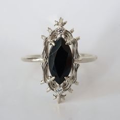 an oval shaped black diamond surrounded by leaves and flowers on a silver ring with white diamonds