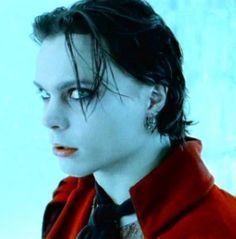 a man with black hair and piercings wearing a red jacket is looking off to the side