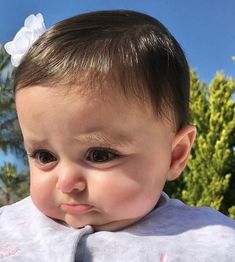 a close up of a baby wearing a bib and looking at the camera with trees in the background