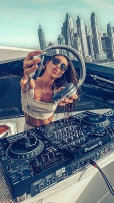 a woman holding a dj's controller in front of a car with a city skyline behind her