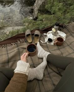 someone is sitting on the ground with their feet up and holding a cup of coffee