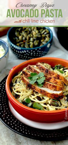 an orange bowl filled with pasta and chicken on top of a table next to other bowls