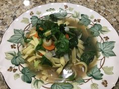 a white plate topped with pasta and veggies on top of a marble counter