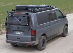 a grey van driving down a dirt road with luggage on the top of it's roof