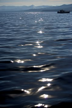 the sun shines on the water as a boat is in the distance with mountains in the background