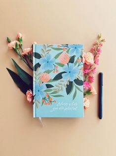 a blue notebook with flowers and a pen on the side next to it that says happy birthday